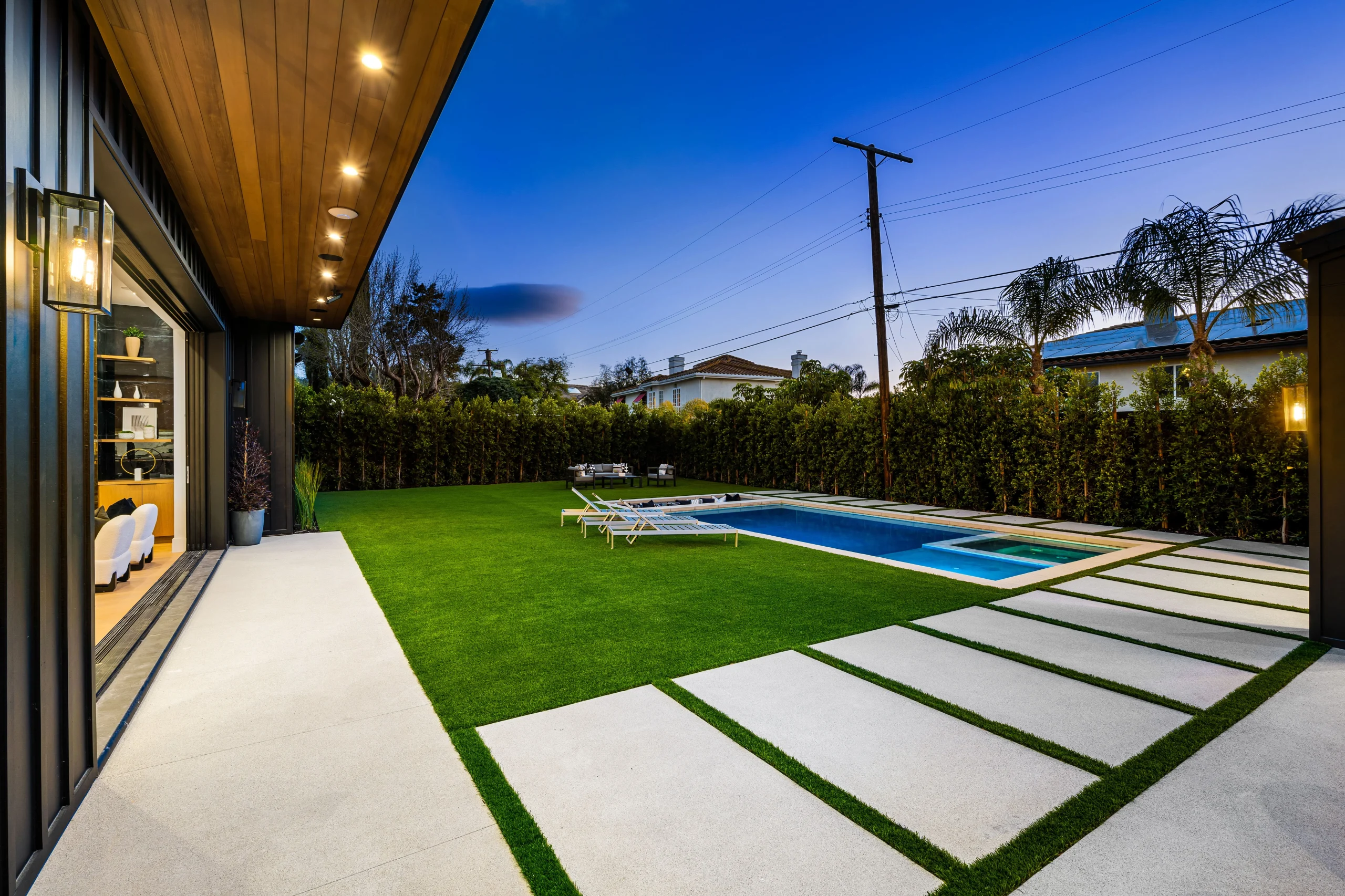 Modern backyard with pool, artificial turf lawn, and concrete stepping path at dusk