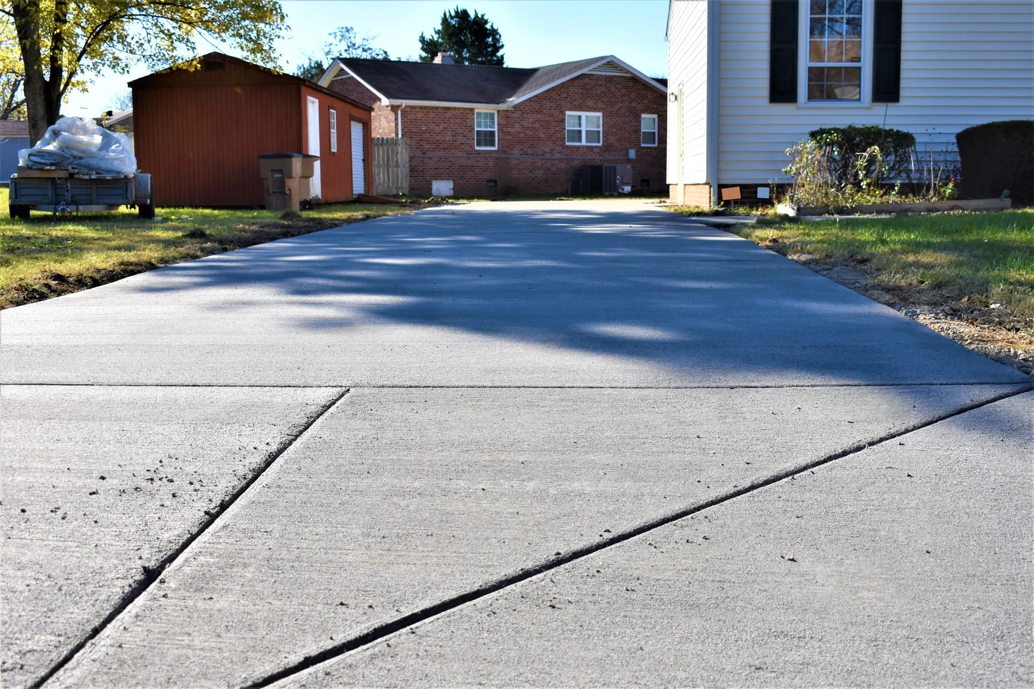 Wide newly installed concrete driveway beside a house and yard with outdoor shed and lawn.