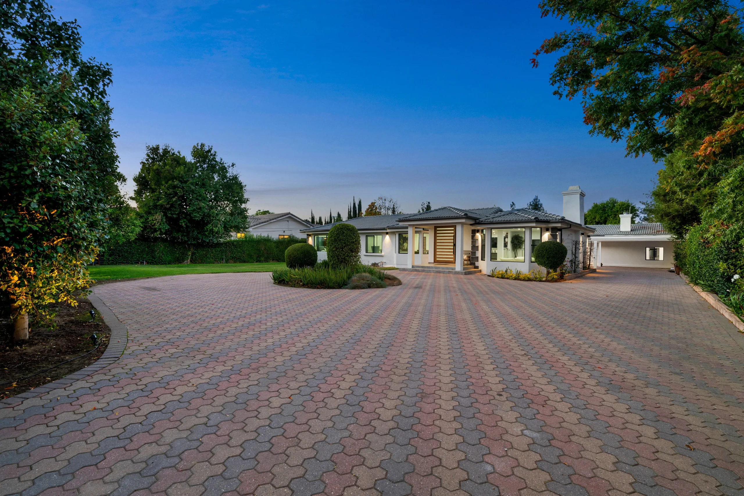 Large residential estate with expansive patterned driveway, manicured landscaping, and modern home exterior in New York.