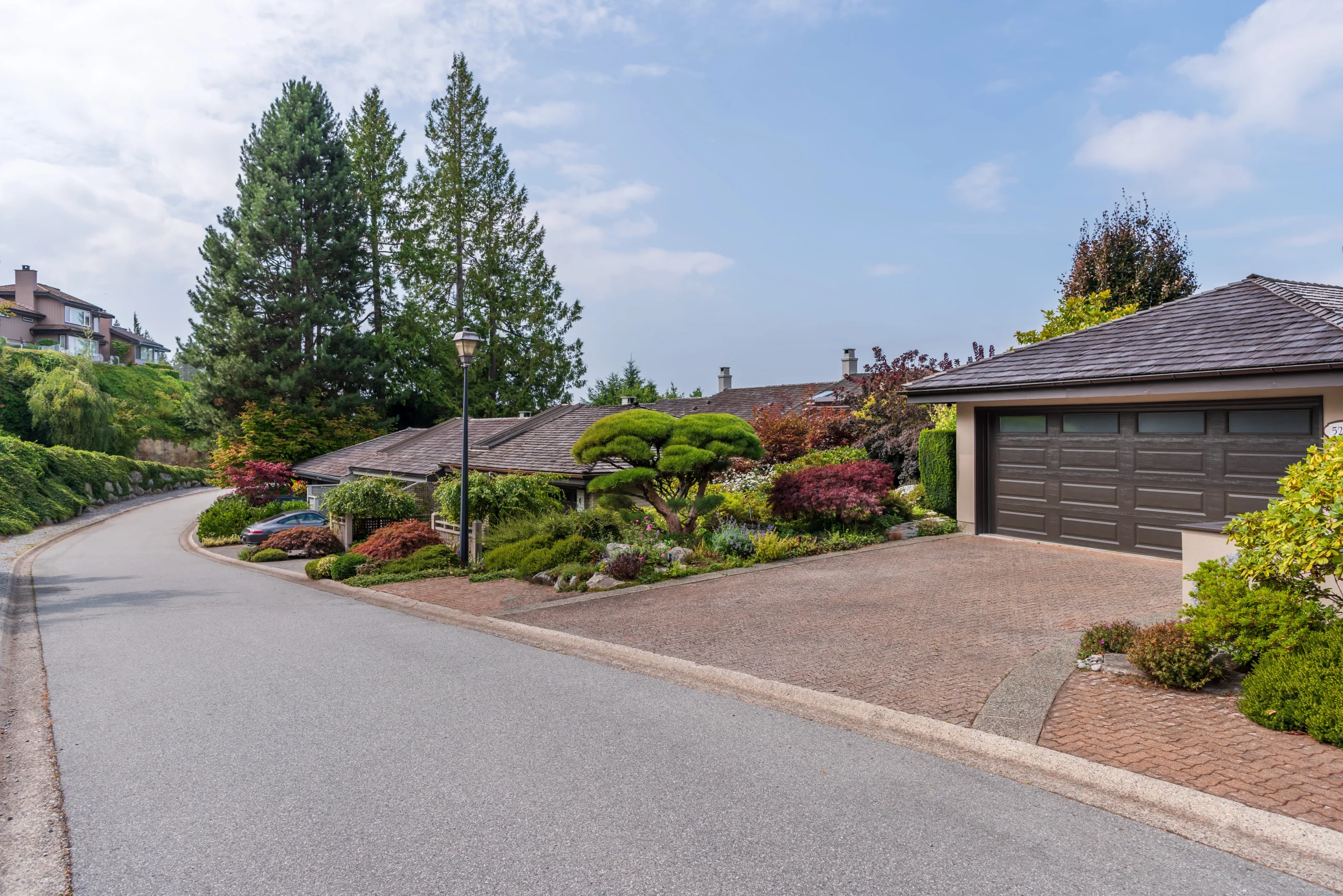 Quiet suburban street with landscaped homes, driveway garages, and mature trees.
