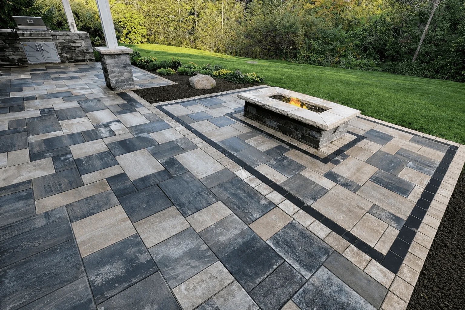 Large paver patio featuring rectangular fire pit, outdoor grill area, and landscaped lawn.