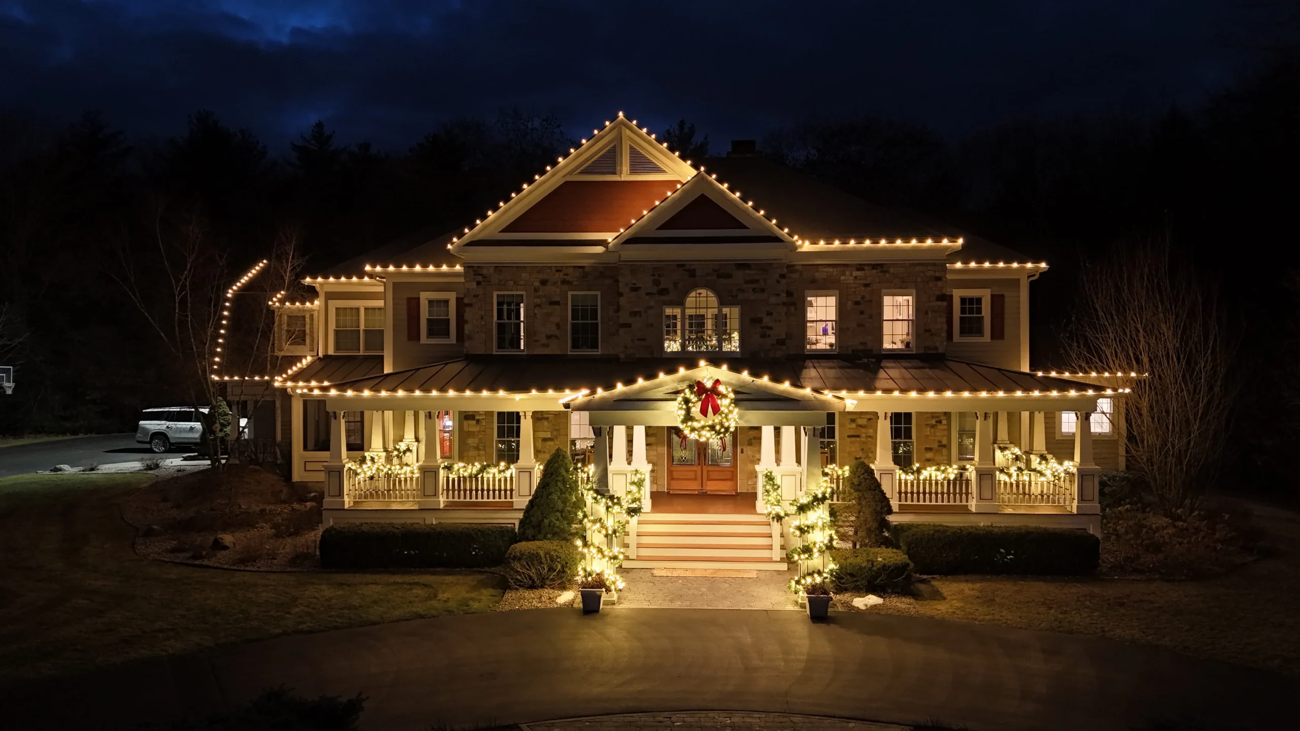Large home decorated with Christmas lights, wreath, and festive holiday decorations during nighttime.