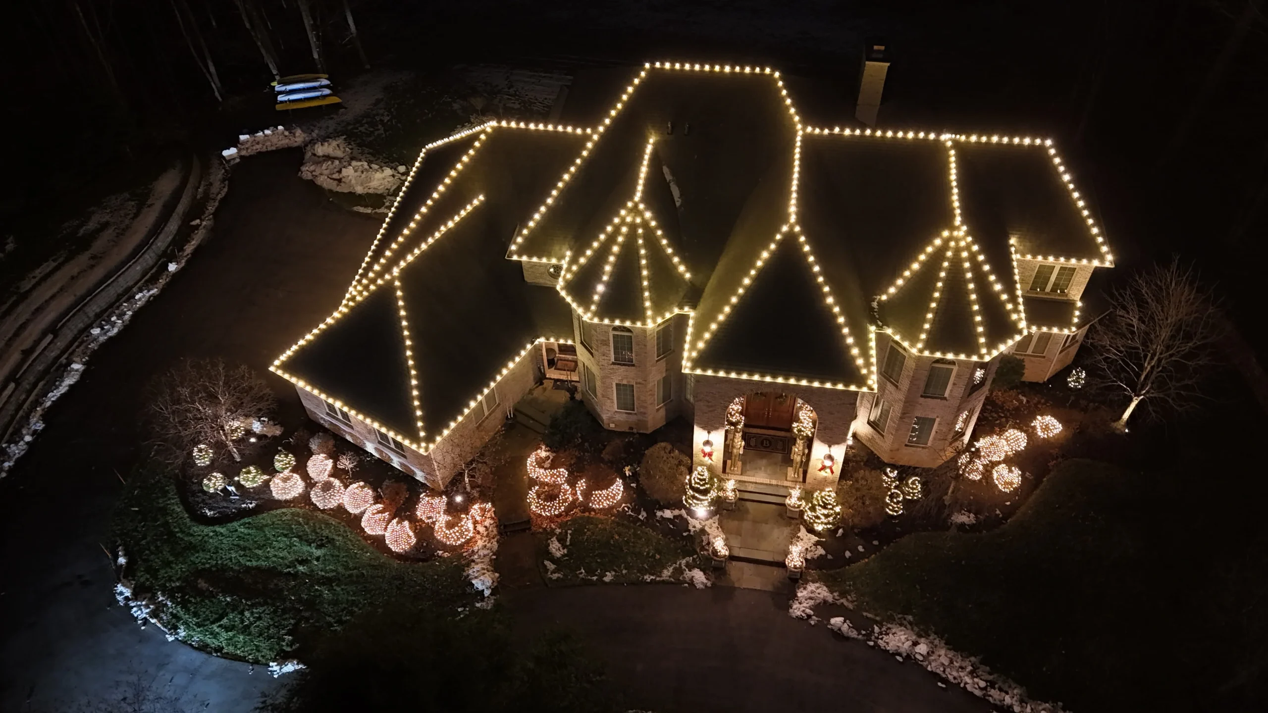 Drone view of a luxury home decorated with Christmas lights outlining the roof and holiday yard decorations.
