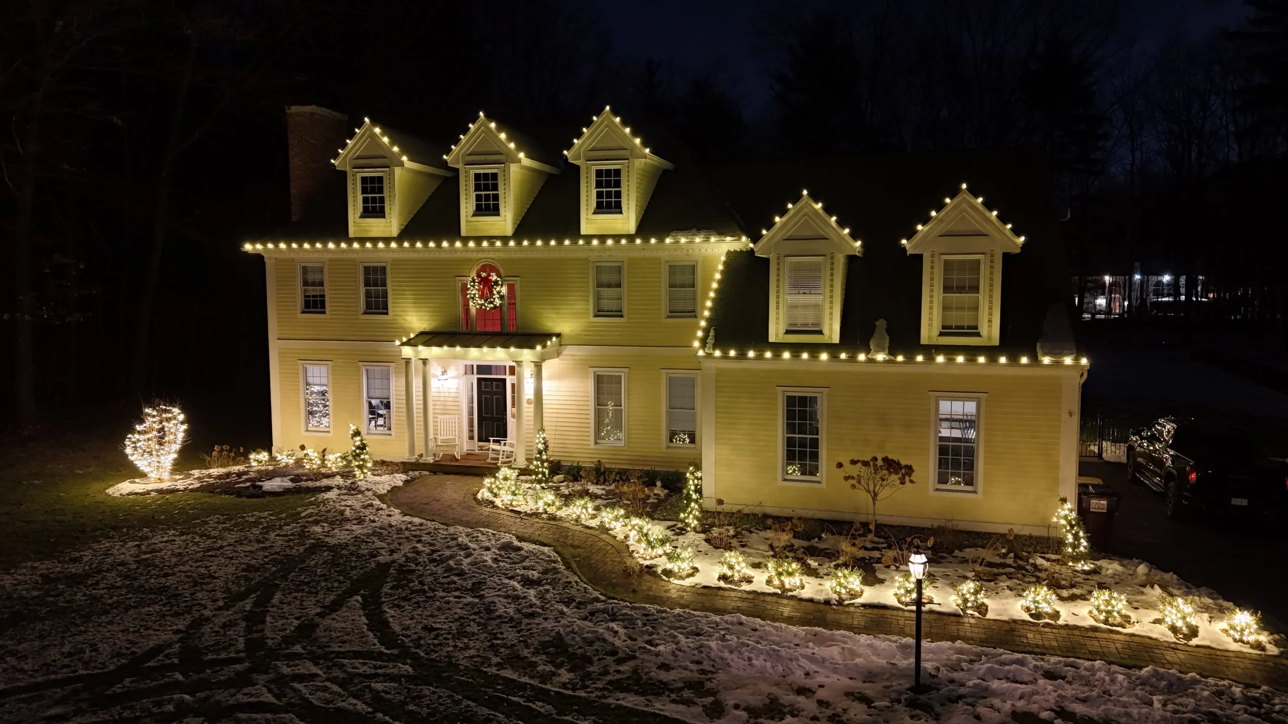 Snow-covered home glowing with Christmas lights and holiday decorations during a winter evening.