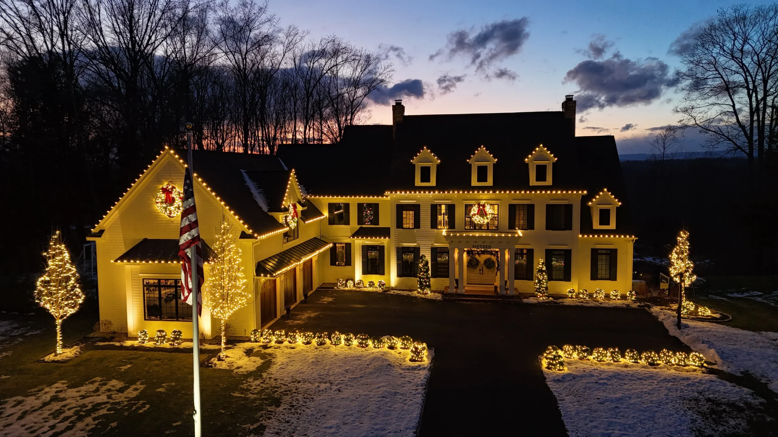 Elegant home decorated with Christmas lights, wreaths, and illuminated trees during a winter evening.