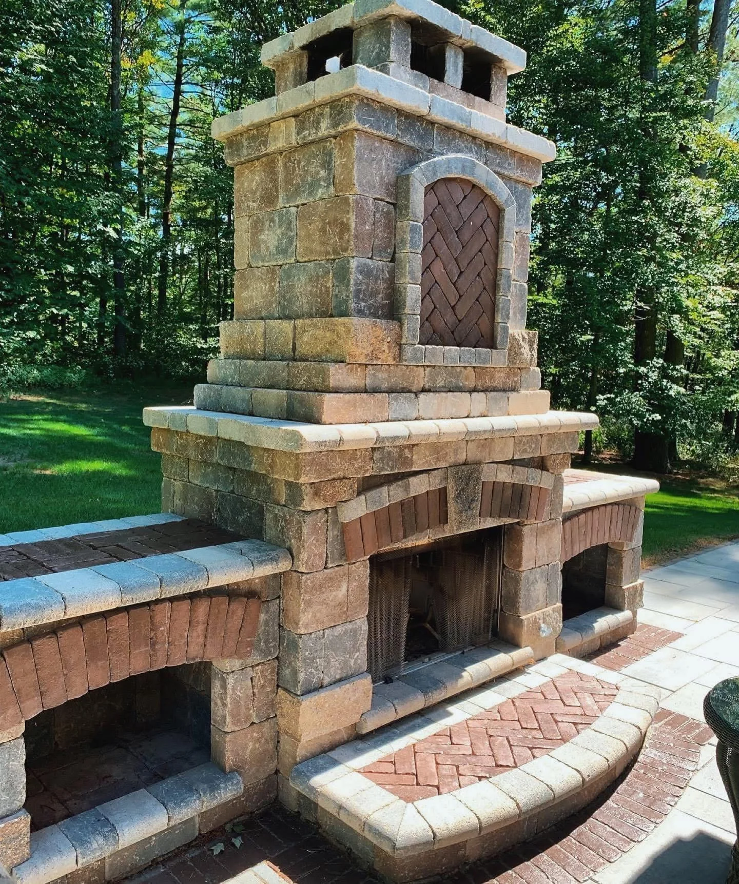 Rustic outdoor masonry fireplace with stone structure and brick patio surround.
