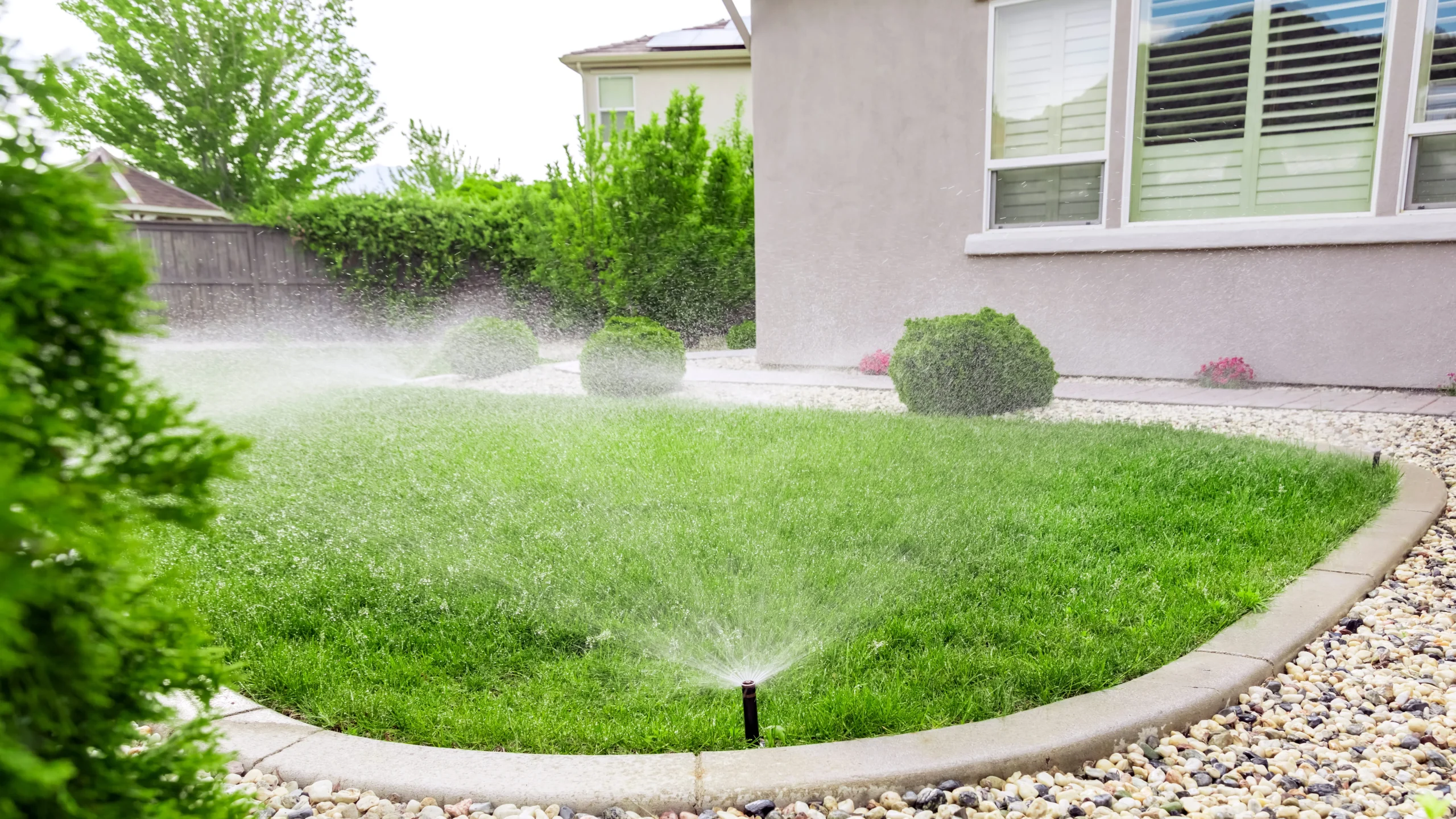 Automatic irrigation system spraying water across a landscaped backyard lawn in New York.