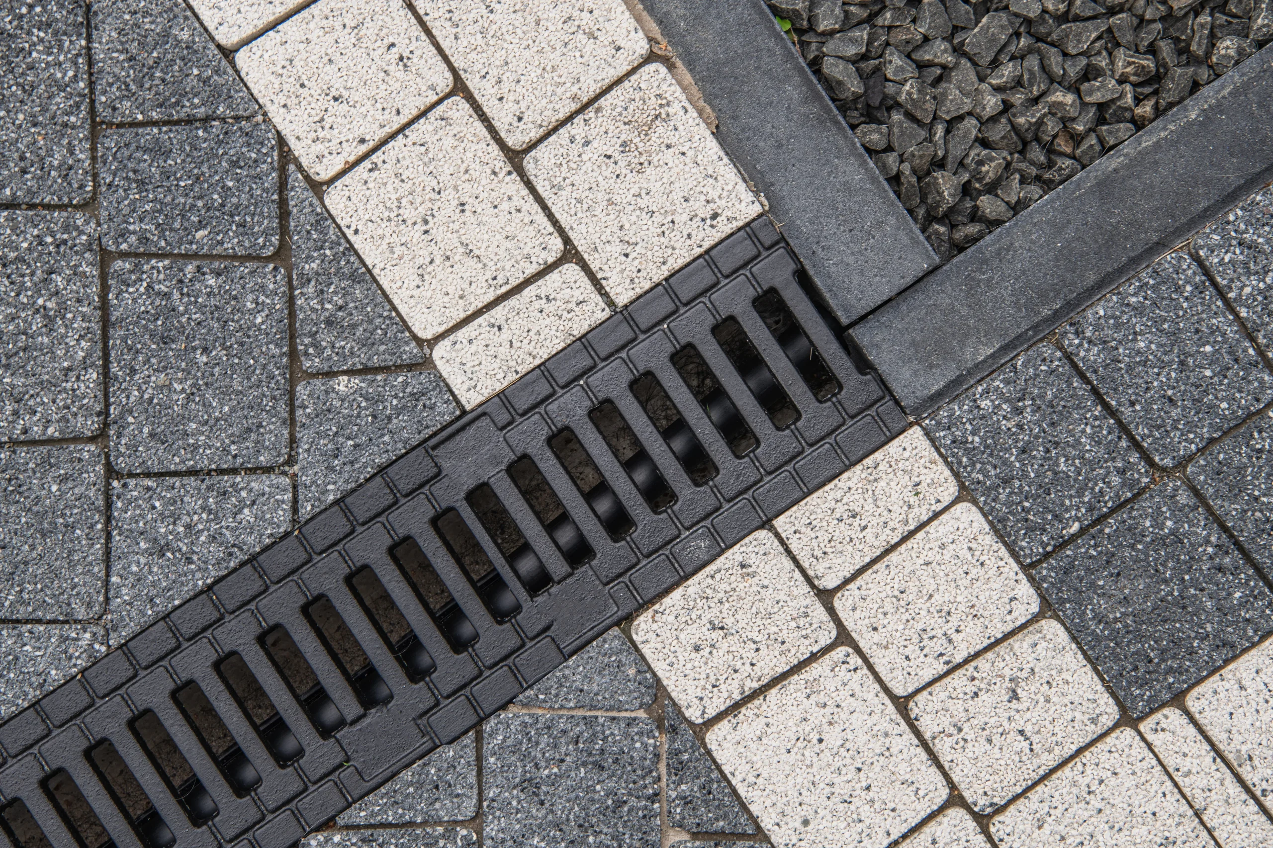 Close-up of a rectangular drainage grate installed across a paved patio with gray and white stone tiles.