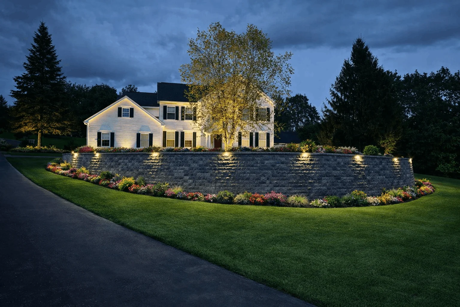 Outdoor lighting highlighting a curved retaining wall, garden beds, and house exterior at night.