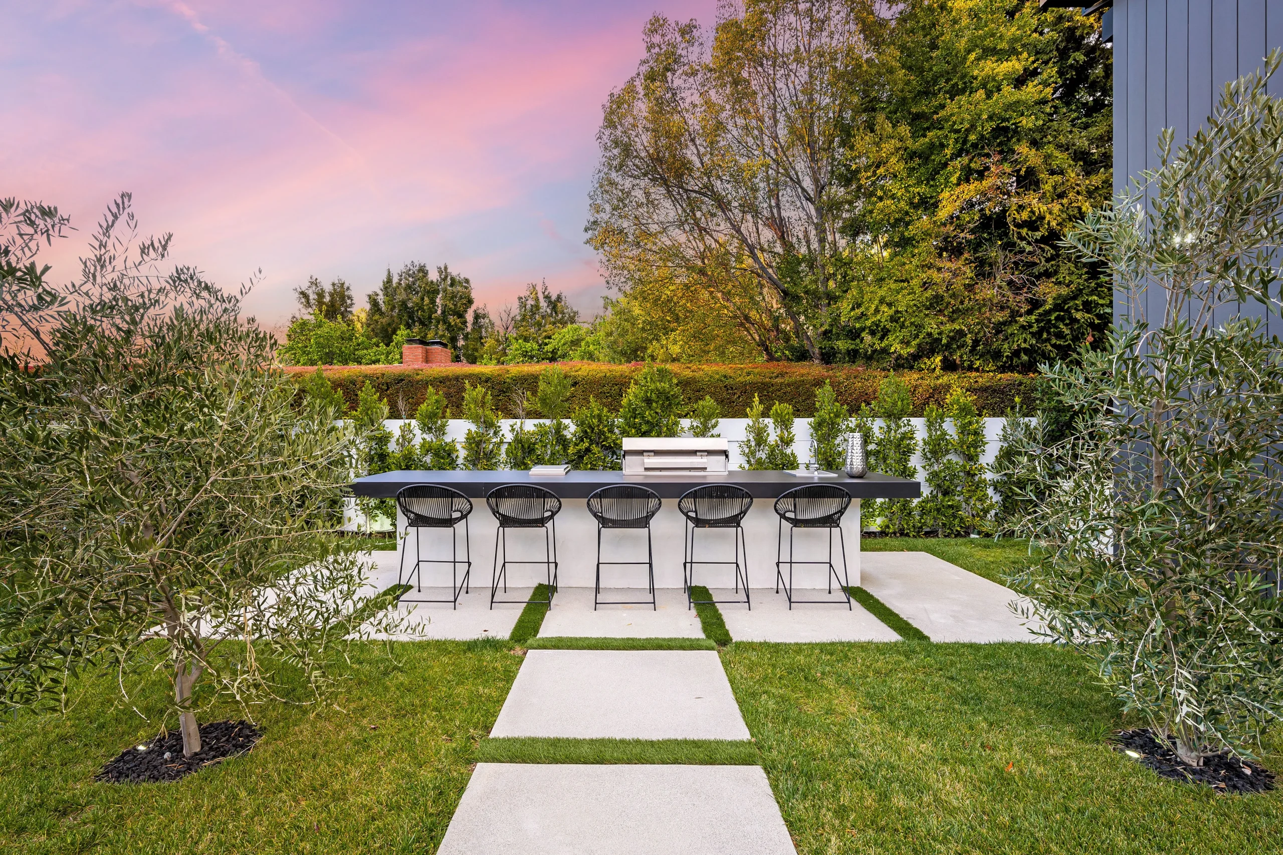 Modern backyard patio with outdoor bar seating, grill station, and landscaped greenery in New York.
