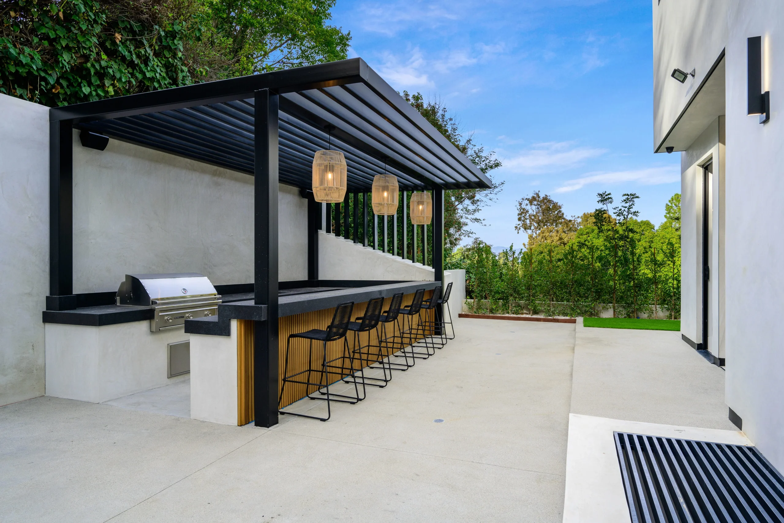 Outdoor bar and grill area with pergola roof, pendant lights, and bar stools on patio.