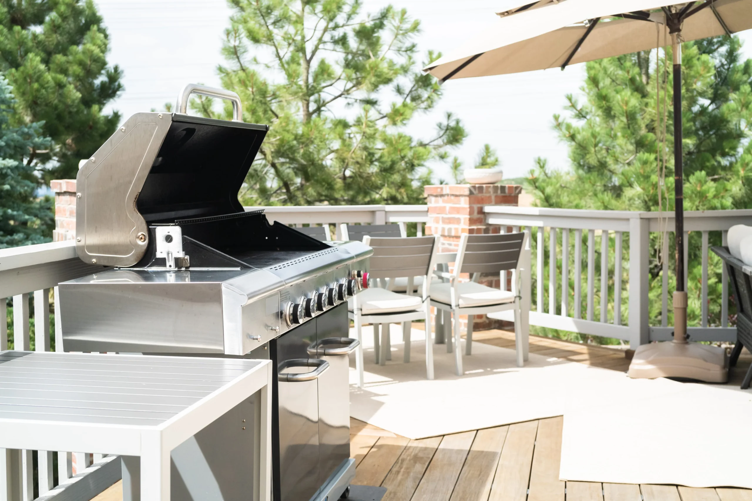 Outdoor deck with stainless steel gas grill, patio dining table, and umbrella seating area.