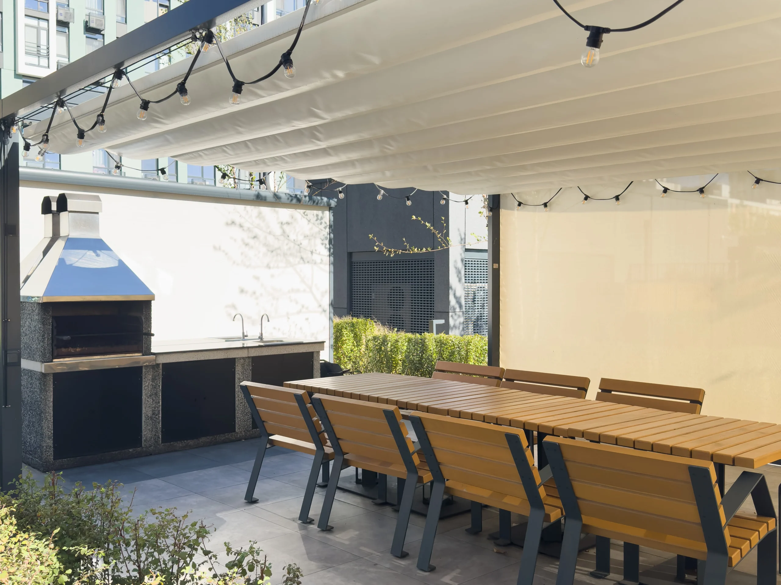 Modern outdoor dining patio with pergola canopy, string lights, wooden table, and built-in grill.