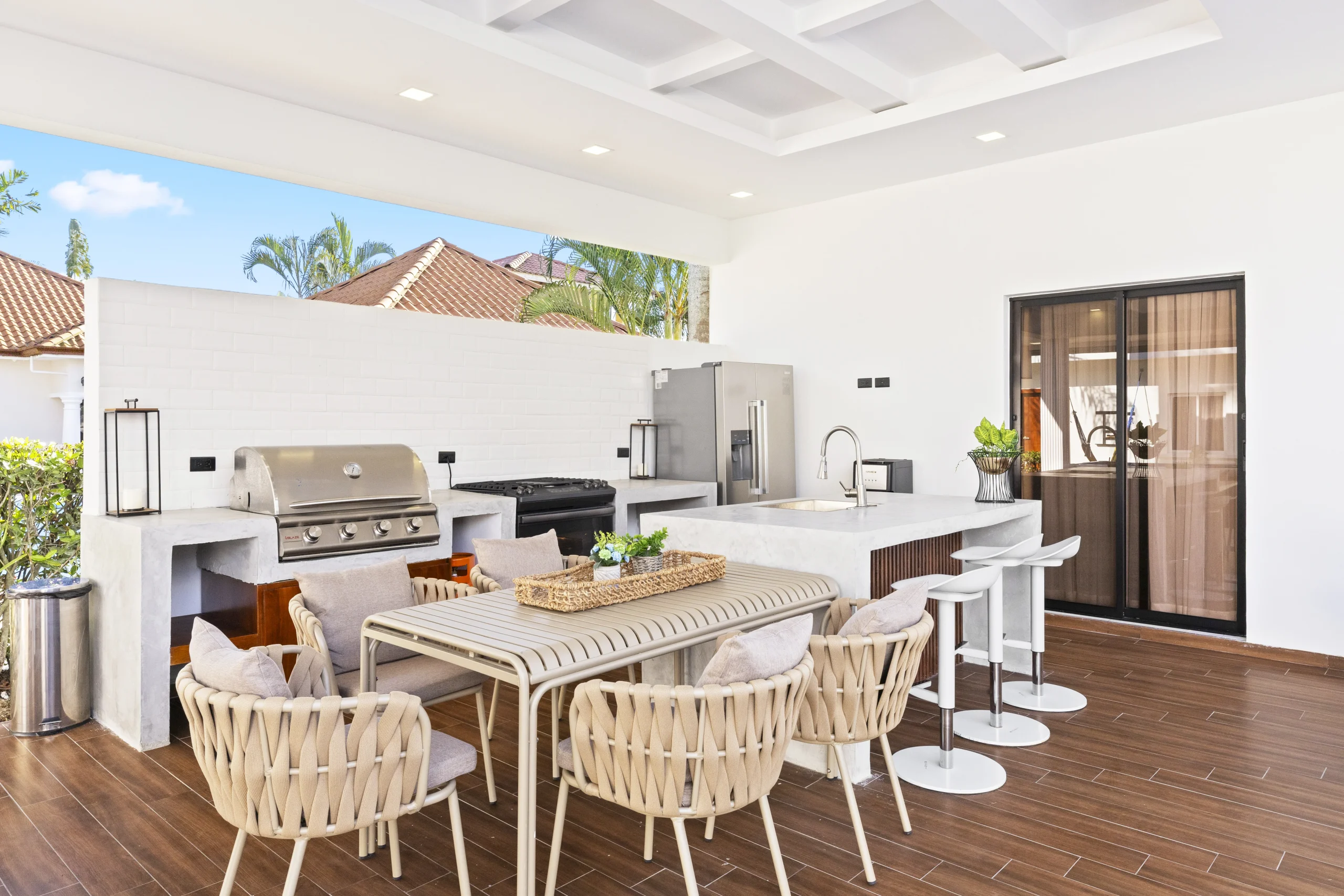 Covered outdoor kitchen with grill, dining table, and bar seating in a modern patio space.