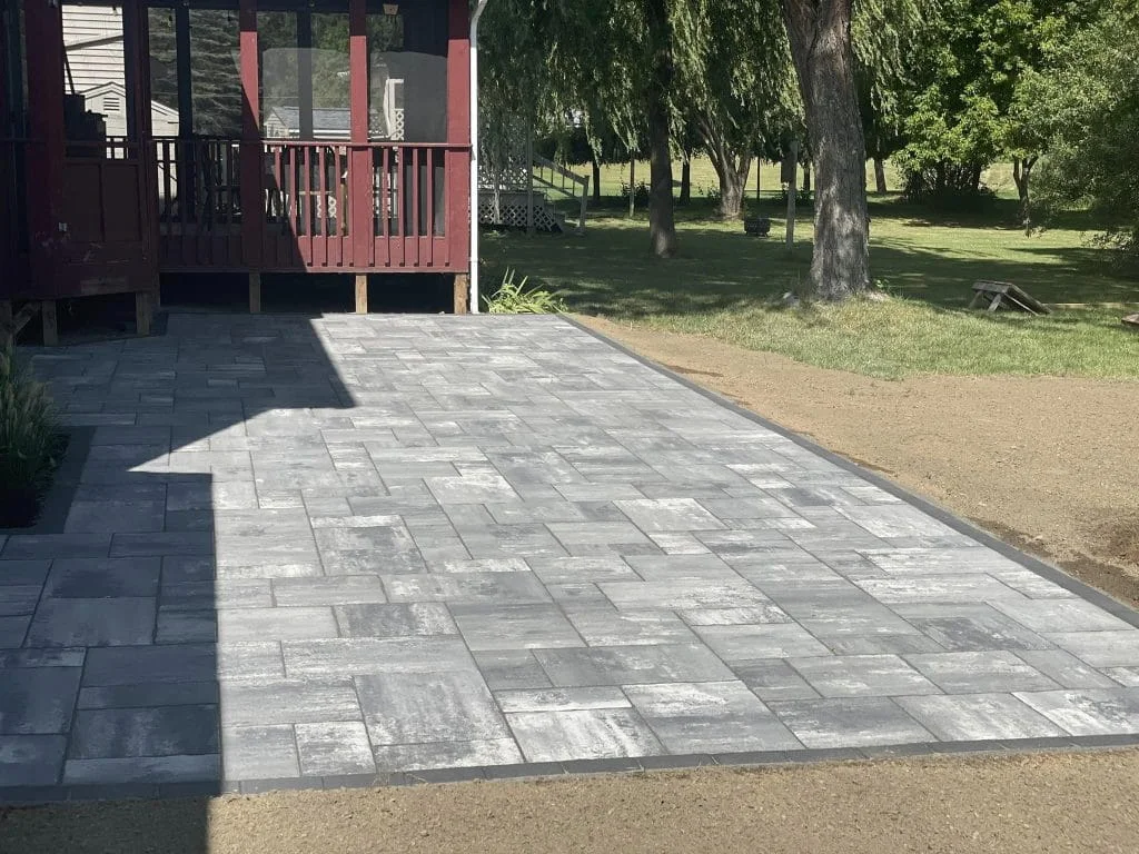 Newly installed gray paver patio beside wooden deck with surrounding yard