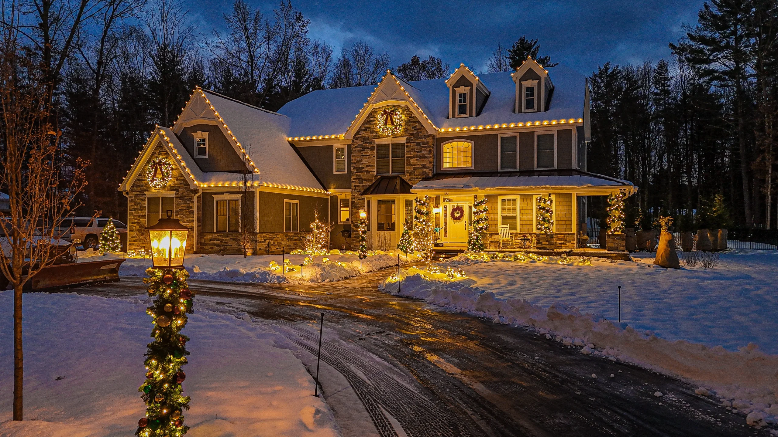Snowy house beautifully decorated with Christmas lights, wreaths, and holiday decorations at night.