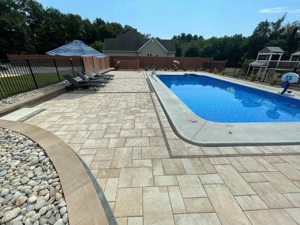 Large paver pool deck with lounge chairs, curved edging, and decorative stone border
