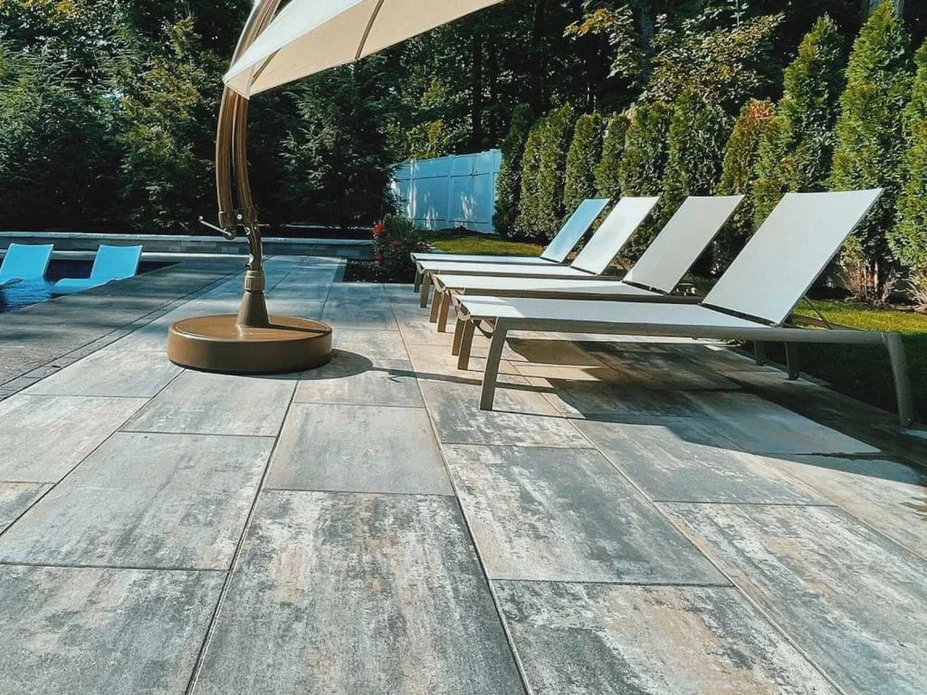 Modern poolside patio with large format pavers, lounge chairs, and cantilever umbrella