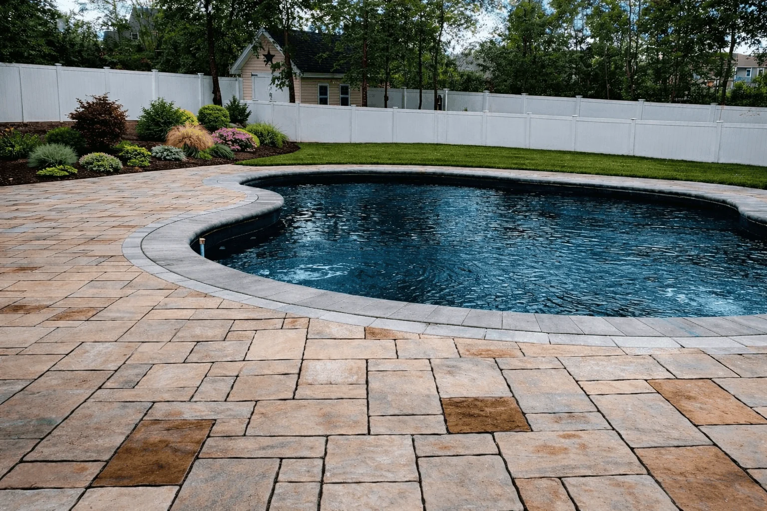 Backyard swimming pool with curved edge, multi-size paver deck, and garden bed along fence