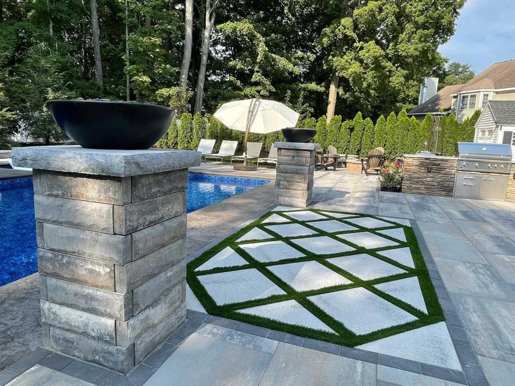 Backyard pool area featuring decorative grid pavers, lounge seating, and stone column accents