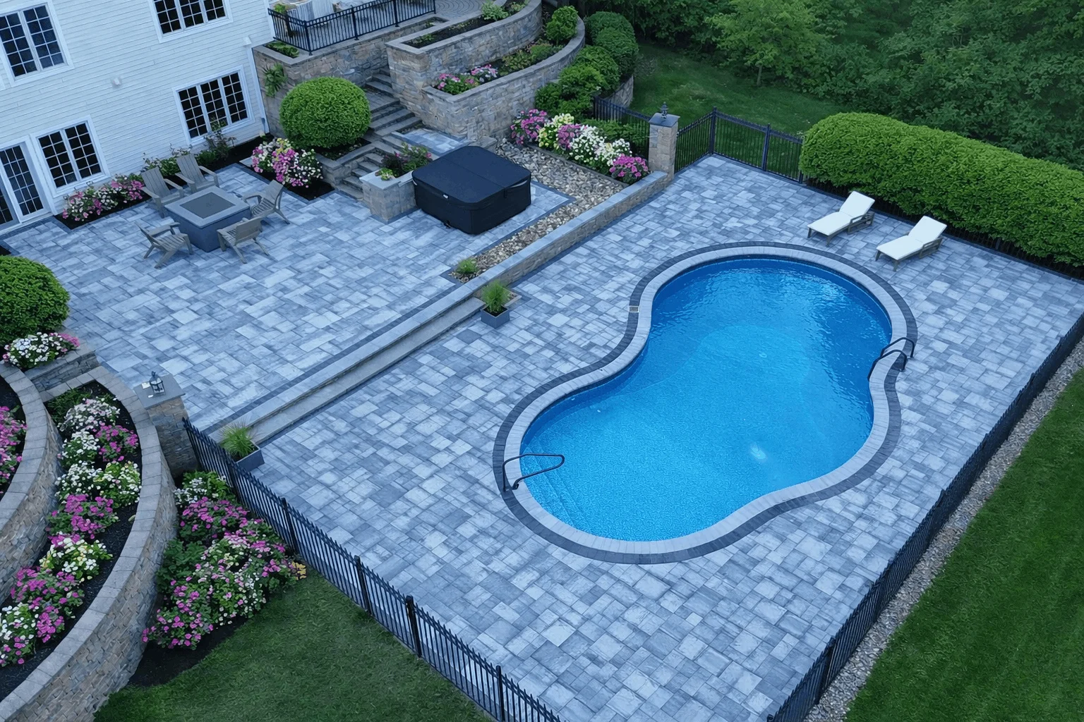 Aerial view of backyard with freeform pool, expansive paver patio, seating areas, and landscaped retaining walls