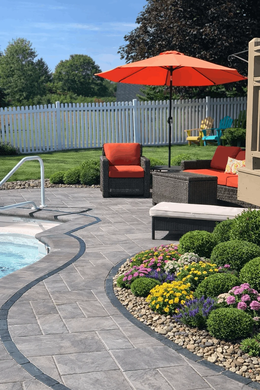 Backyard pool deck with curved pavers, patio furniture, and vibrant garden border