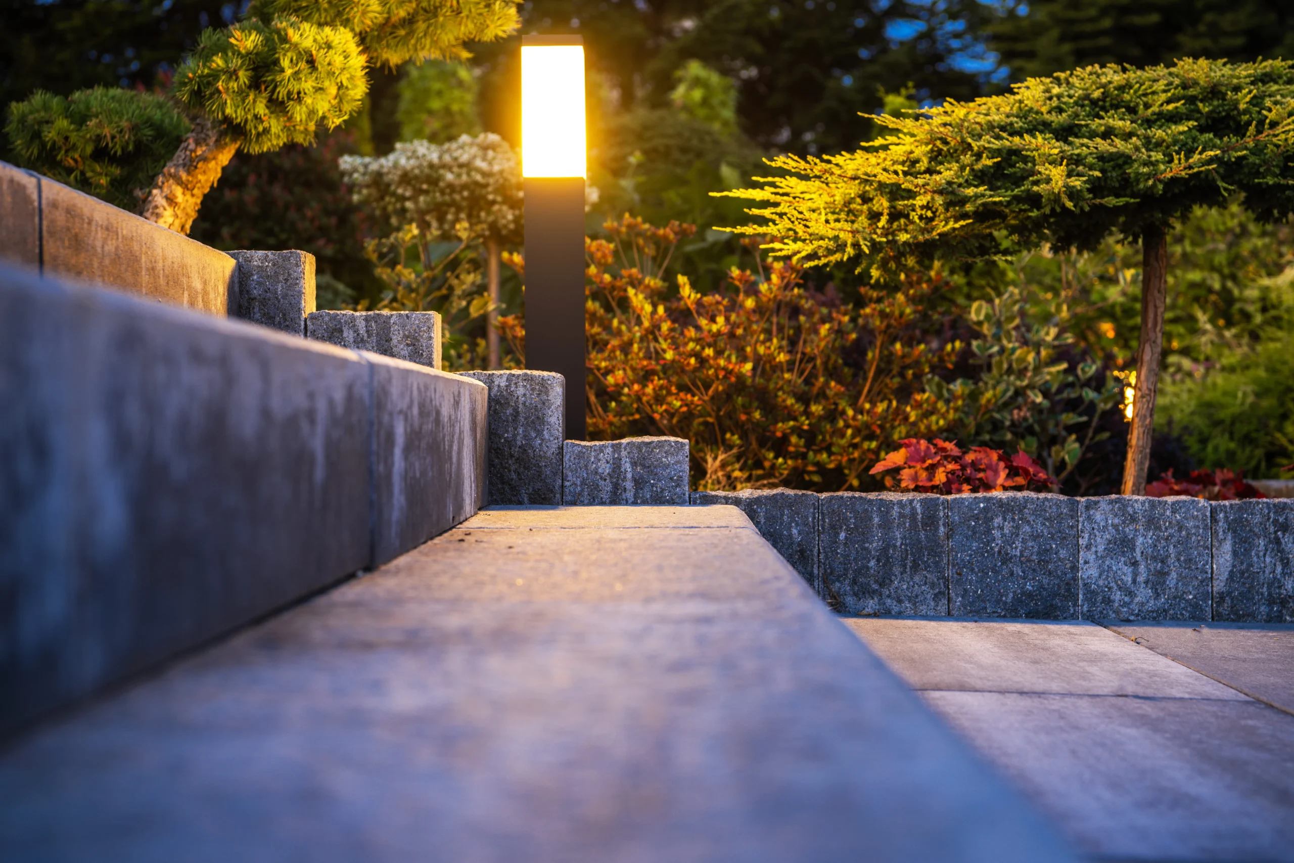Outdoor pathway light illuminating landscaped garden with stone edging and plants.