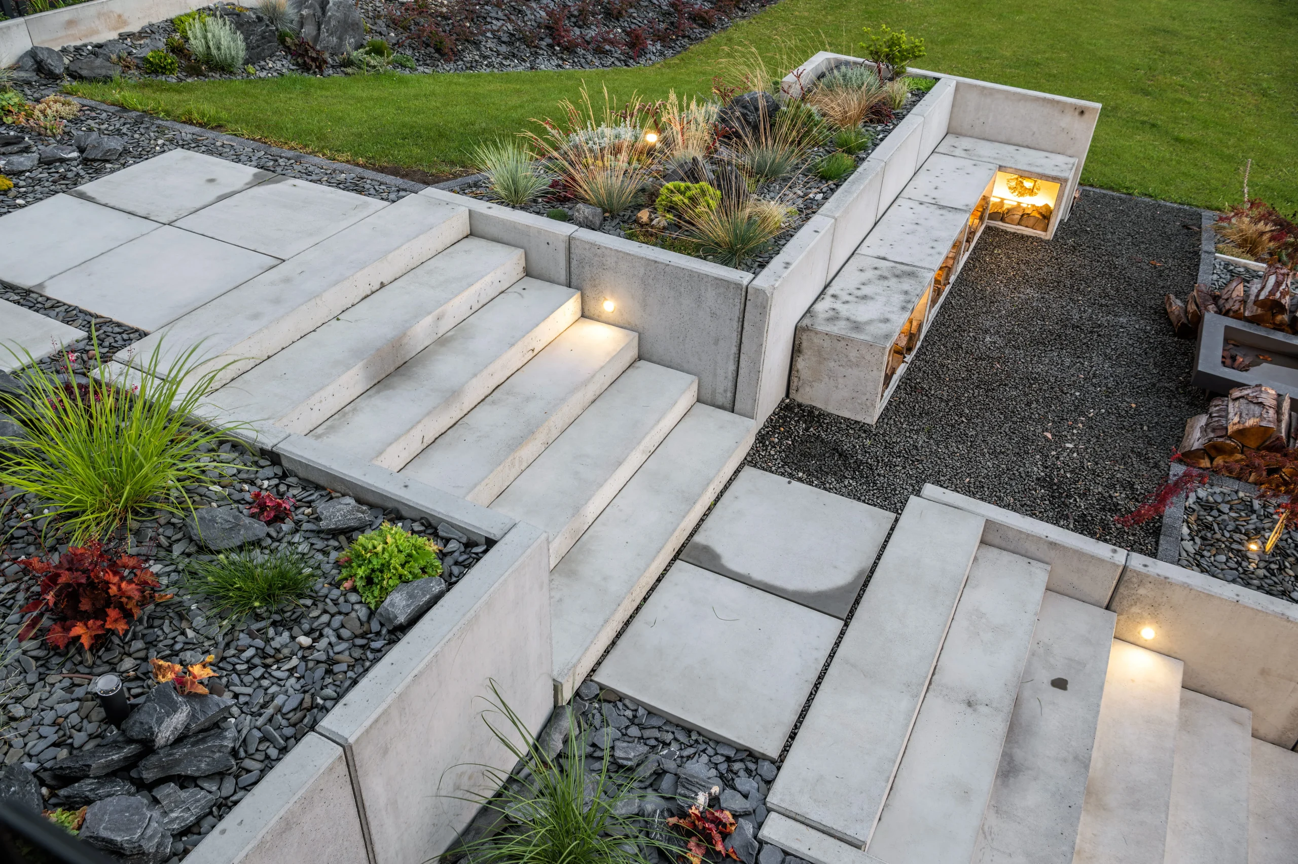 Terraced concrete steps and retaining walls with plants, gravel, and outdoor lighting.
