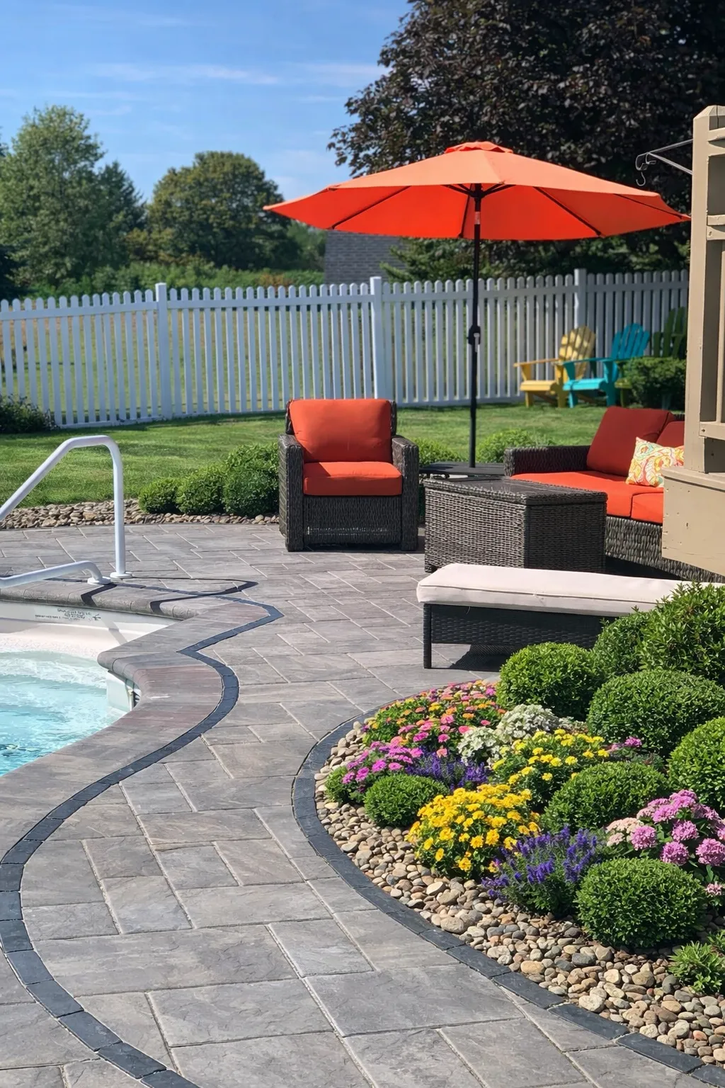 Modern backyard pool patio featuring decorative pavers, garden flowers, outdoor lounge seating, and shaded umbrella in New York