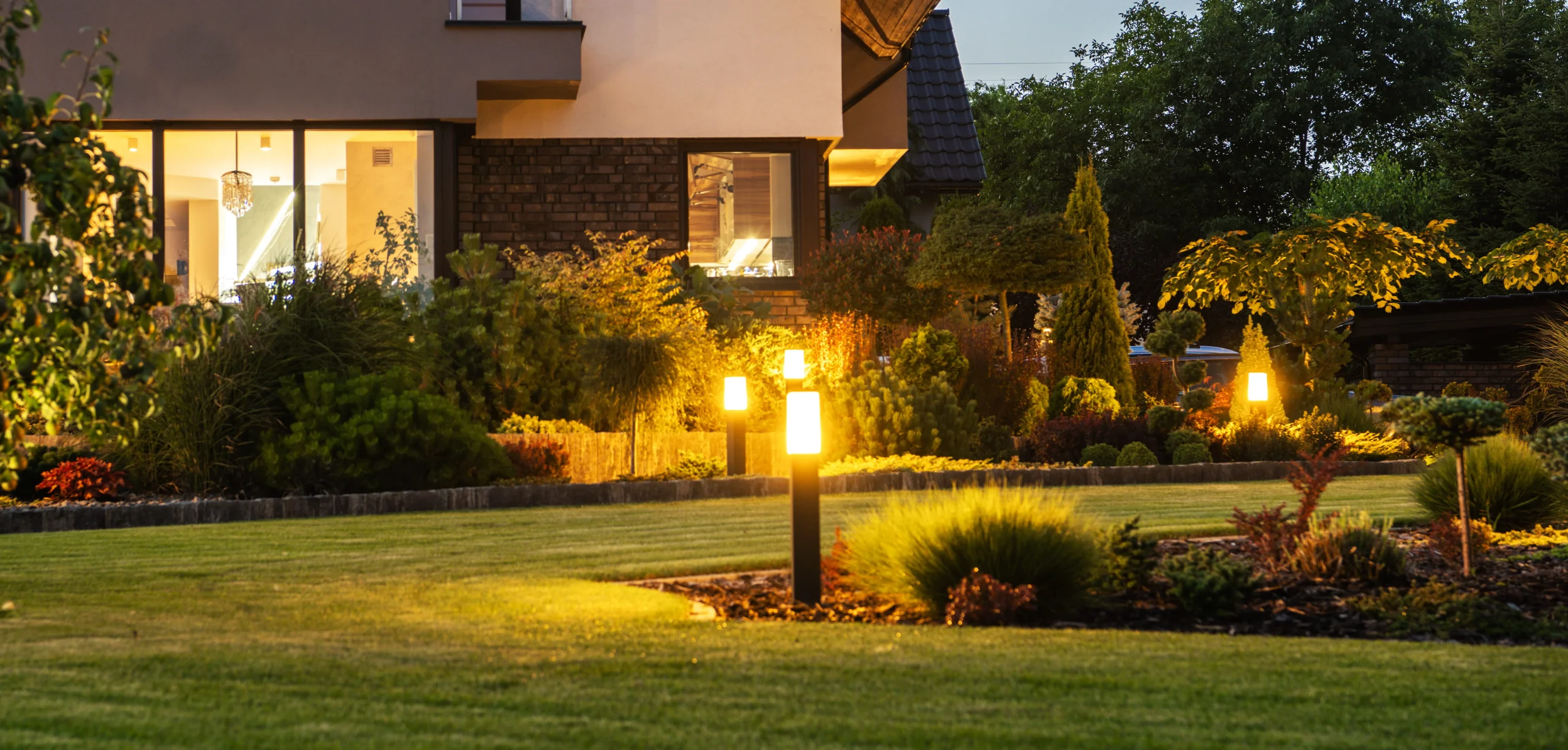 Pathway and landscape lights illuminating shrubs, trees, and lawn around a home at night in New York.